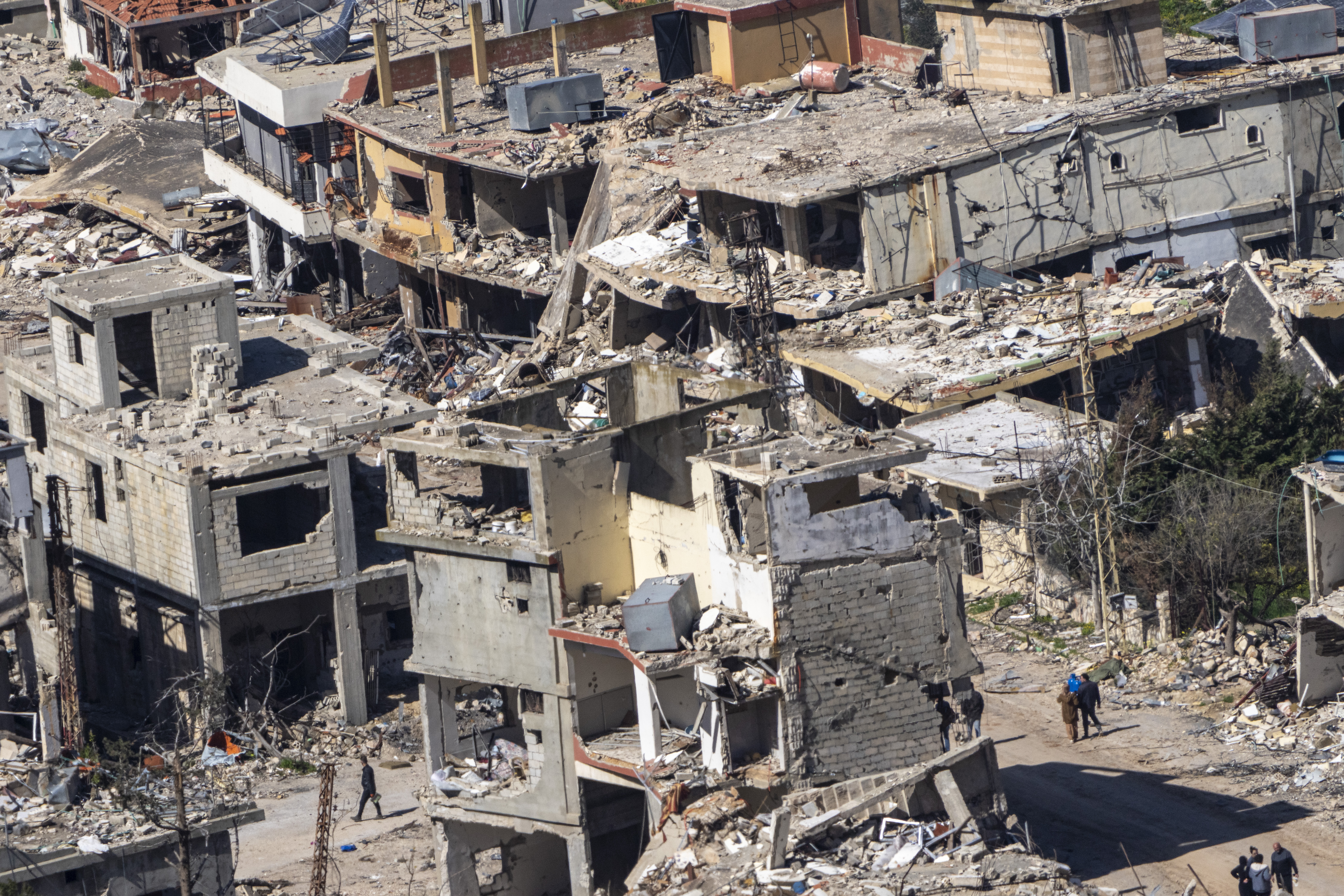 Lebanese walk between buildings destroyed by the Israeli army's air and ground offensive against Hezbollah in the village of Odaisseh after Israeli forces withdrew from border villages in southern Lebanon as seen from Kibbutz Misgav Am, northern Israel, Tuesday, Feb. 18, 2025. (AP Photo/Ariel Schalit)