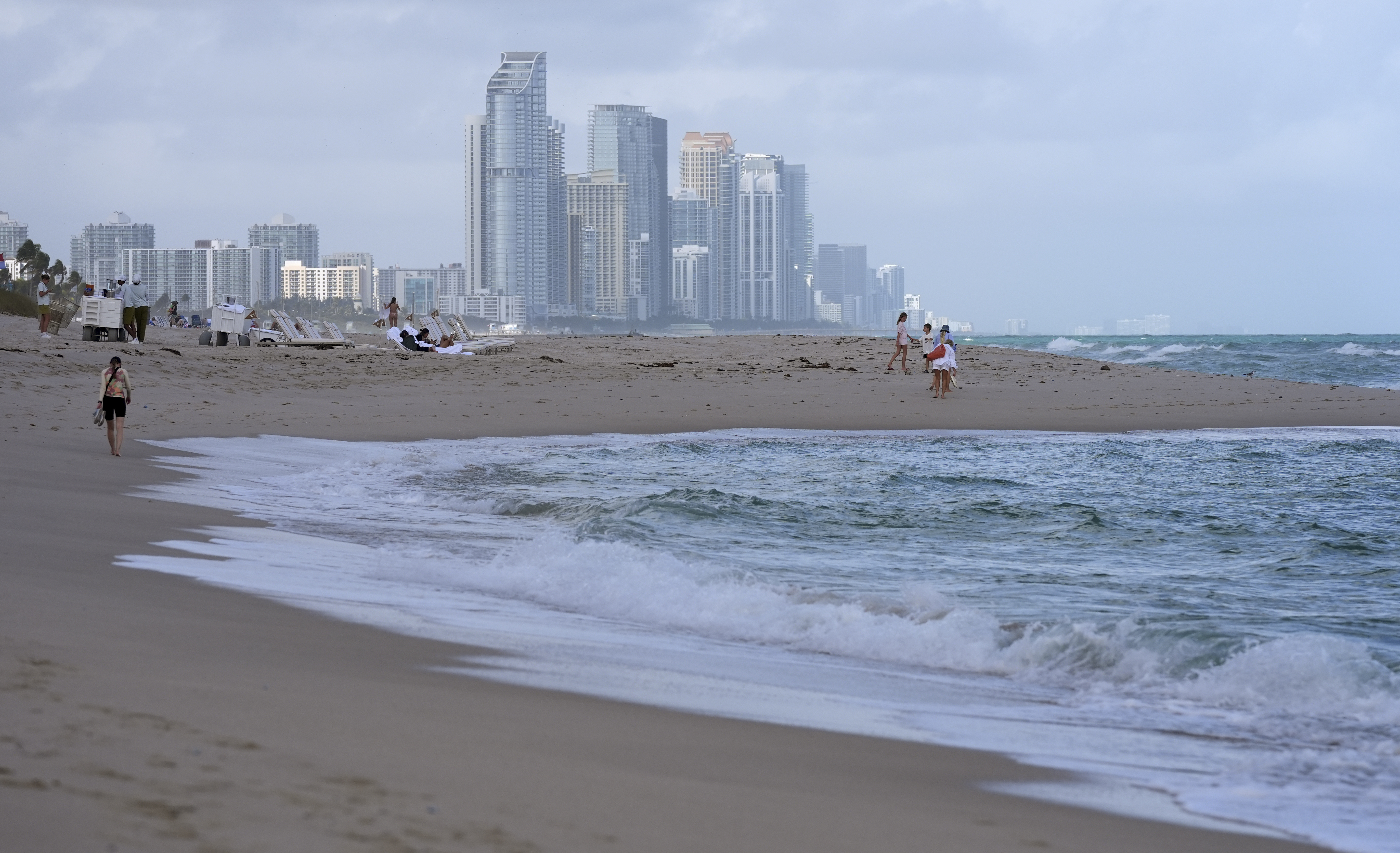 FILE - People walk along the beach in Surfside, Fla., near the skyline of Sunny Isles Beach, Dec. 17, 2024. (AP Photo/Lynne Sladky, file)